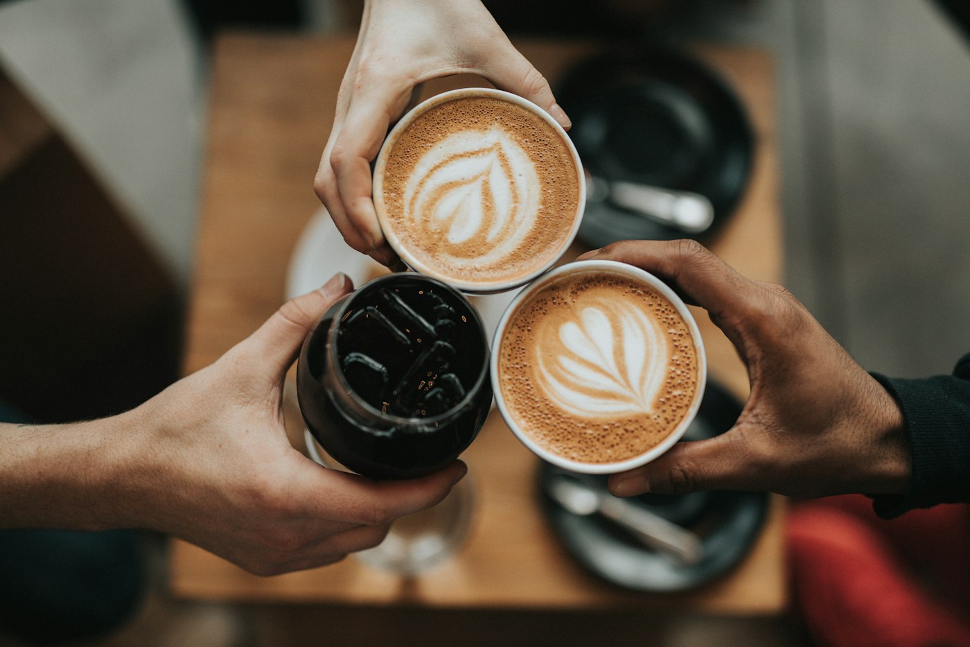 Three friends toasting latte art cups at a cafe table